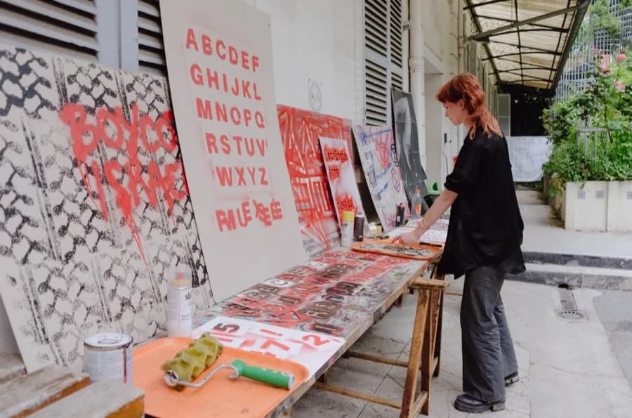 Outdoor workshop: alphabets and slogans painted in red on boards; a person works at a table.