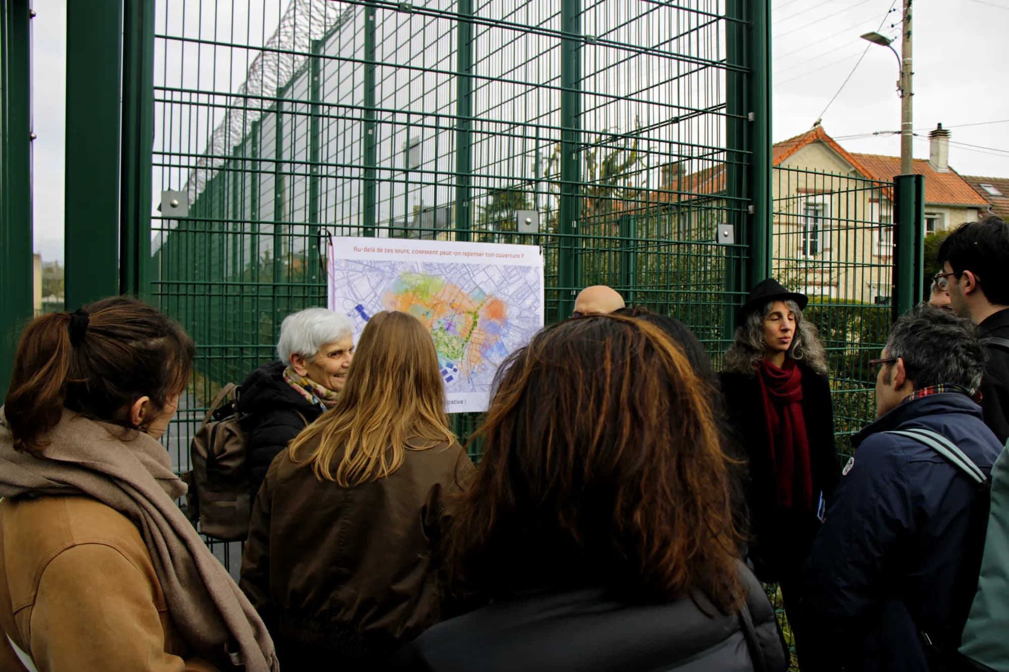 A group gathered in front of the map on the fence, houses of the neighbourhood in the background