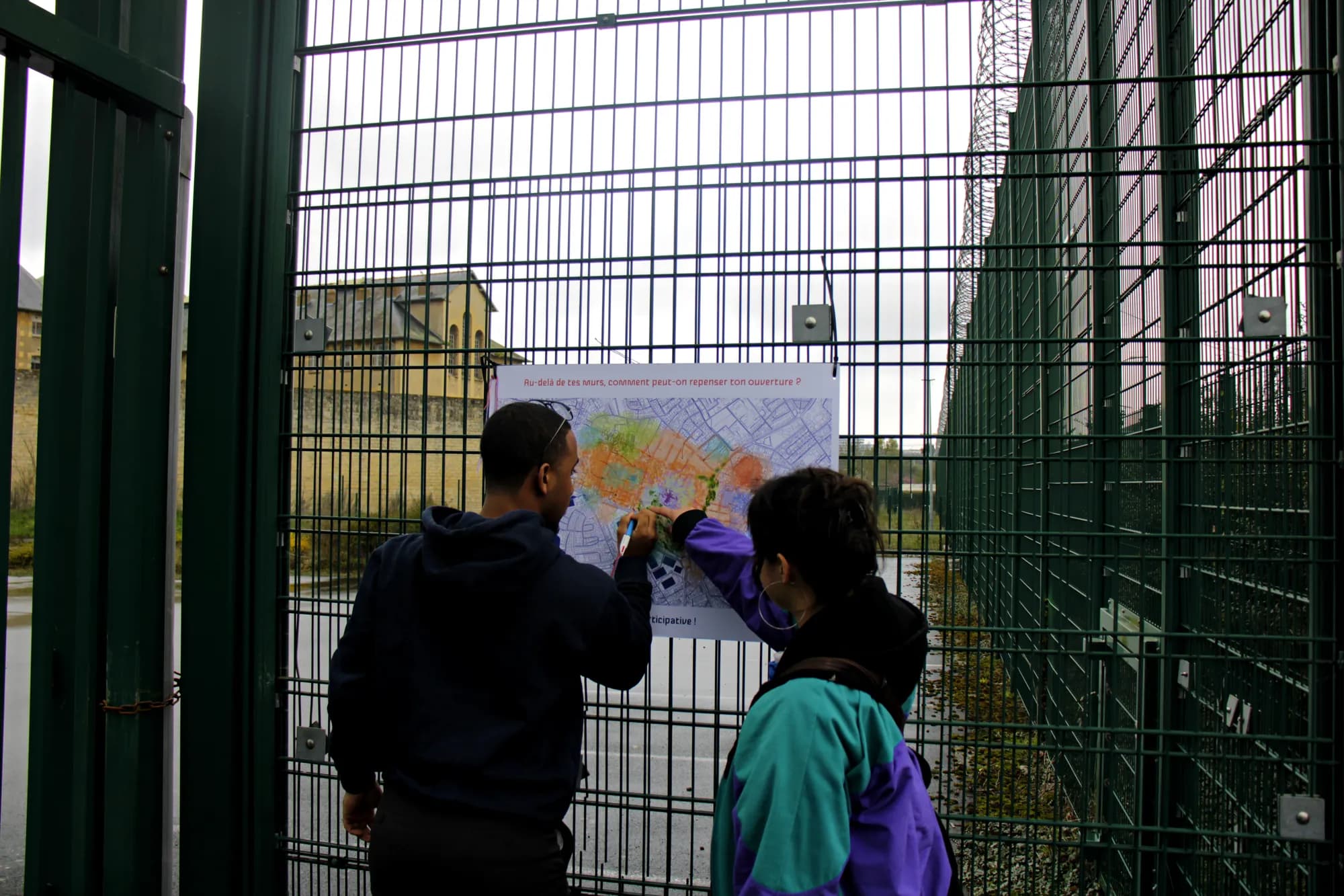 Two people annotate the map hung on the prison fence