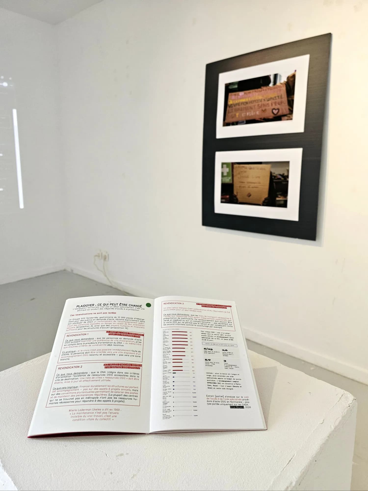 A panel of photographs on the wall and, in front, a booklet open on a white plinth
