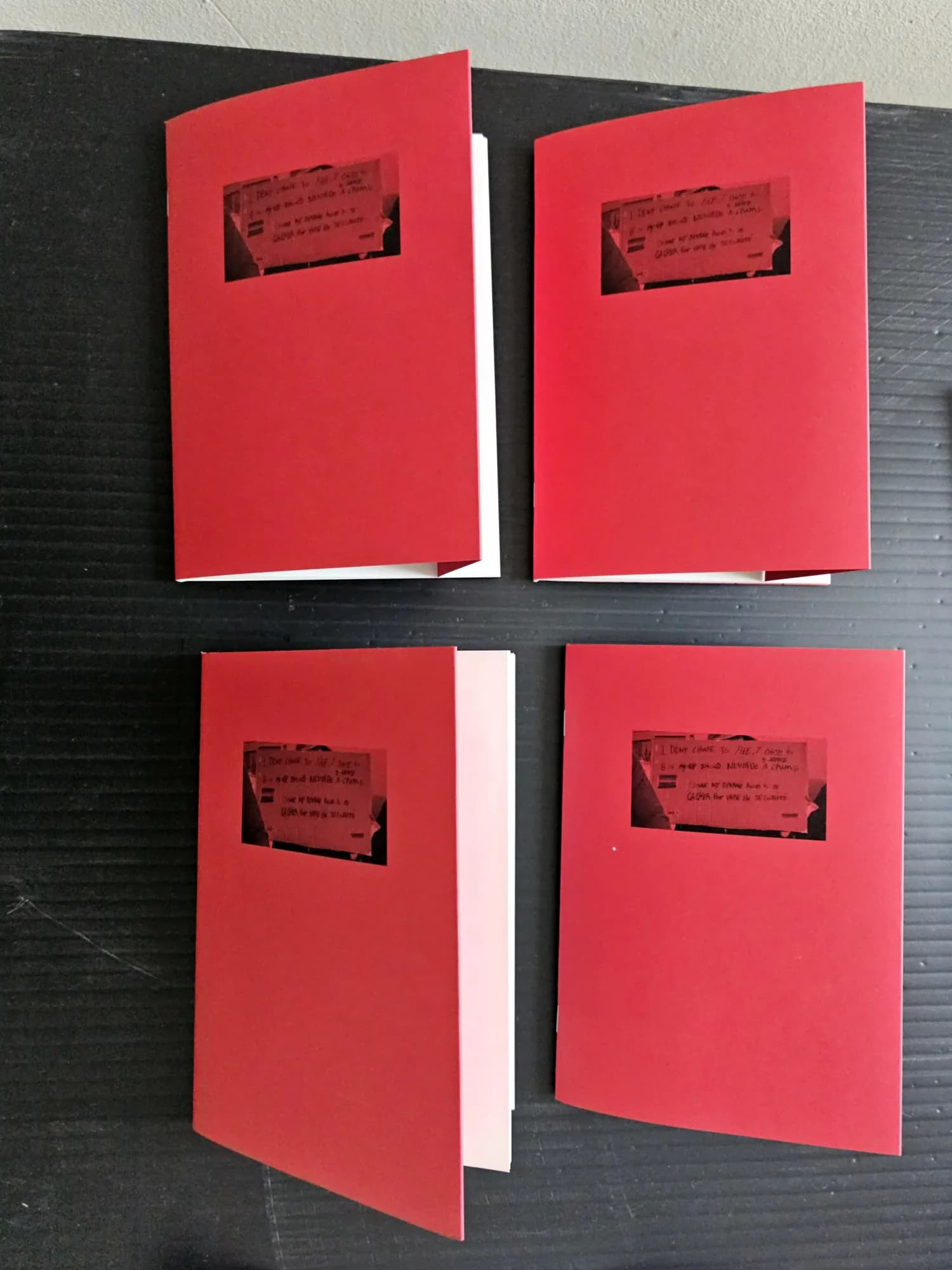 Four red-covered booklets, each with a window onto the photograph of a placard, on black