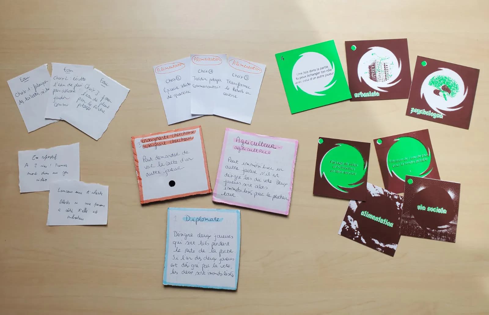 Game prototypes on a table: handwritten cards and printed burgundy and green cards