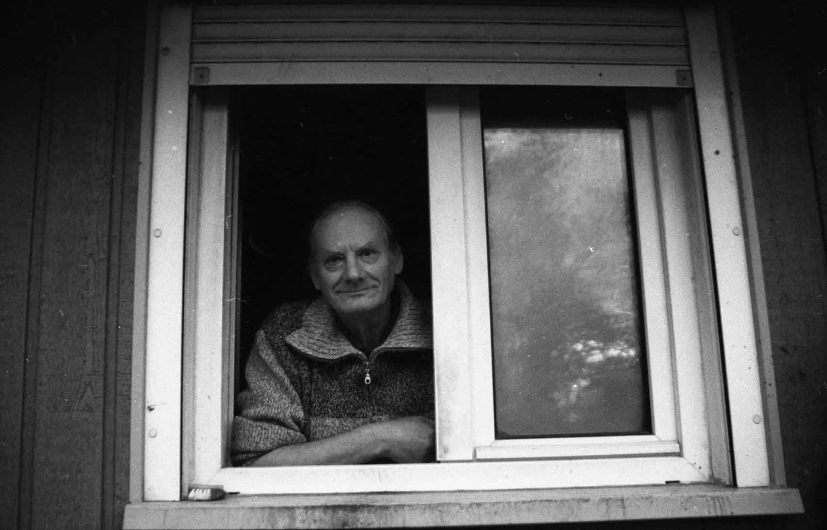 A man leaning on his windowsill smiles at the camera, black and white