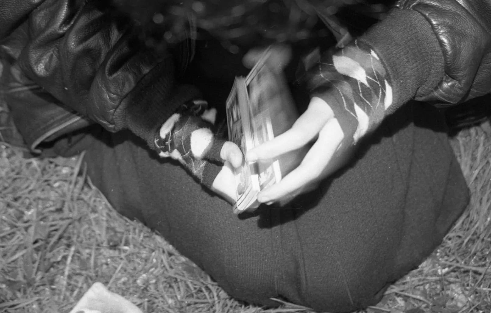Close-up of hands in fingerless gloves holding a deck of cards, lit by flash, black and white