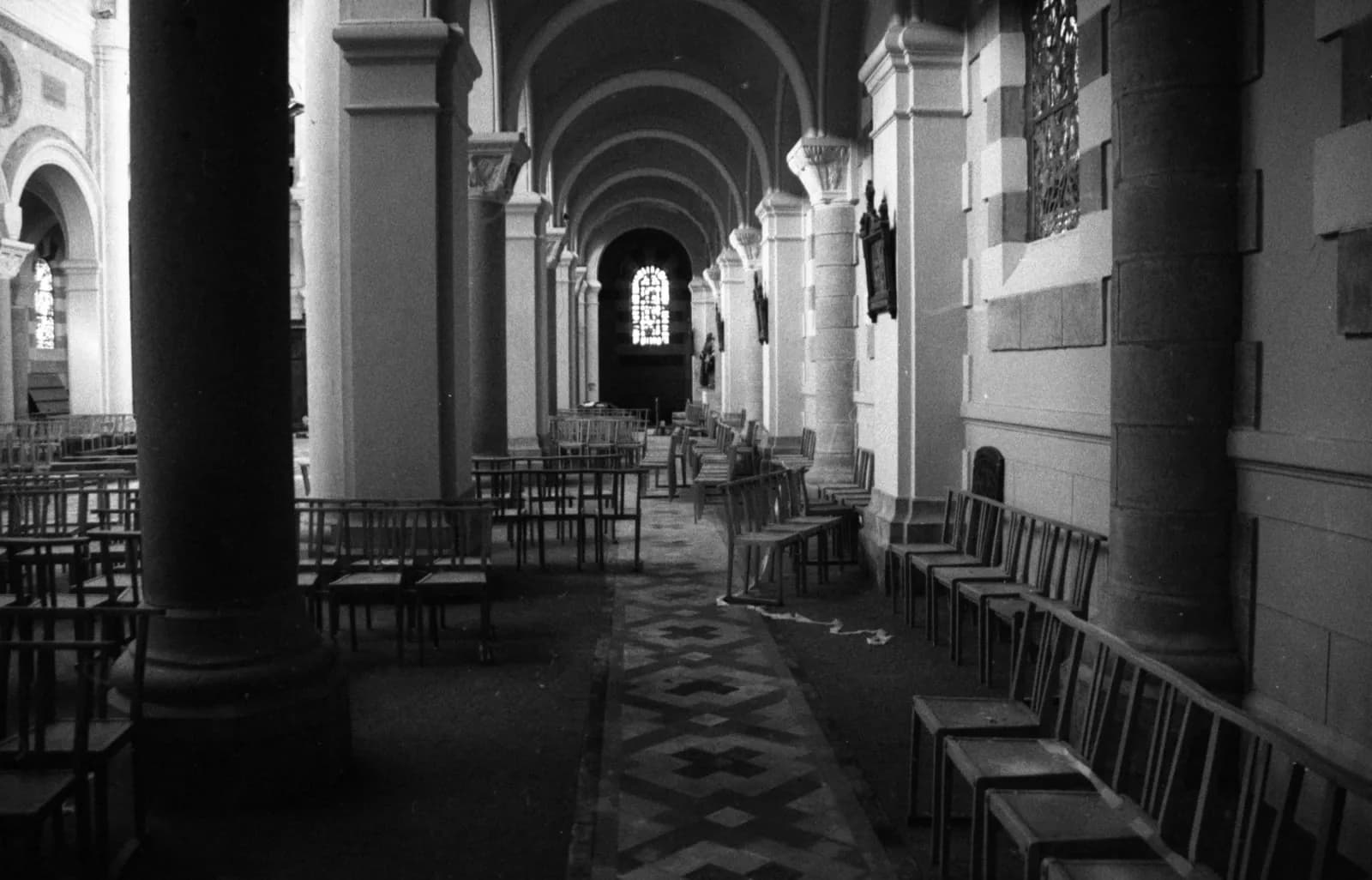 Side aisle of a church: columns, arches and rows of chairs, black and white