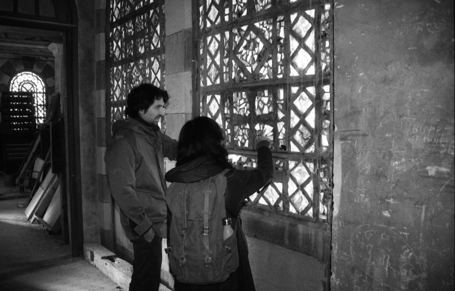 Two people in front of an openwork lattice screen inside a building, black and white