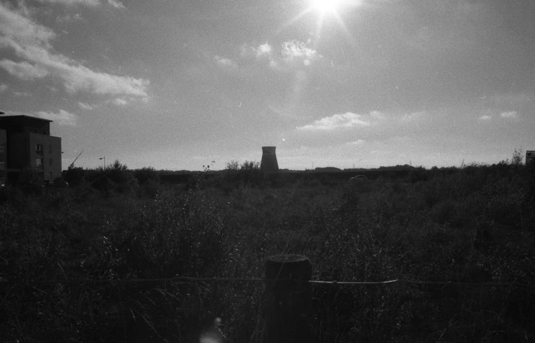 Wasteland against the sun, a cooling tower on the horizon, black and white