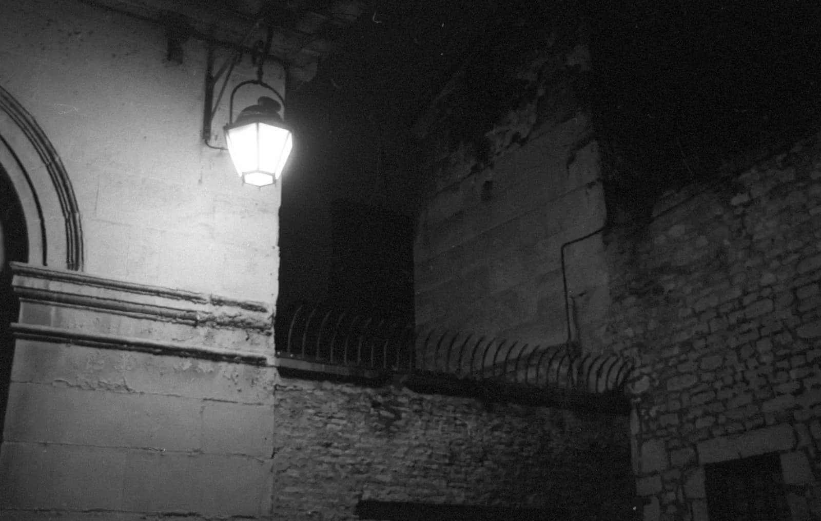 A lit lantern on a stone wall at night, above a railing, black and white